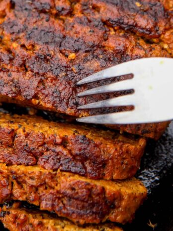 A vegan steak on an iron skillet cut into slices with a fork in it.