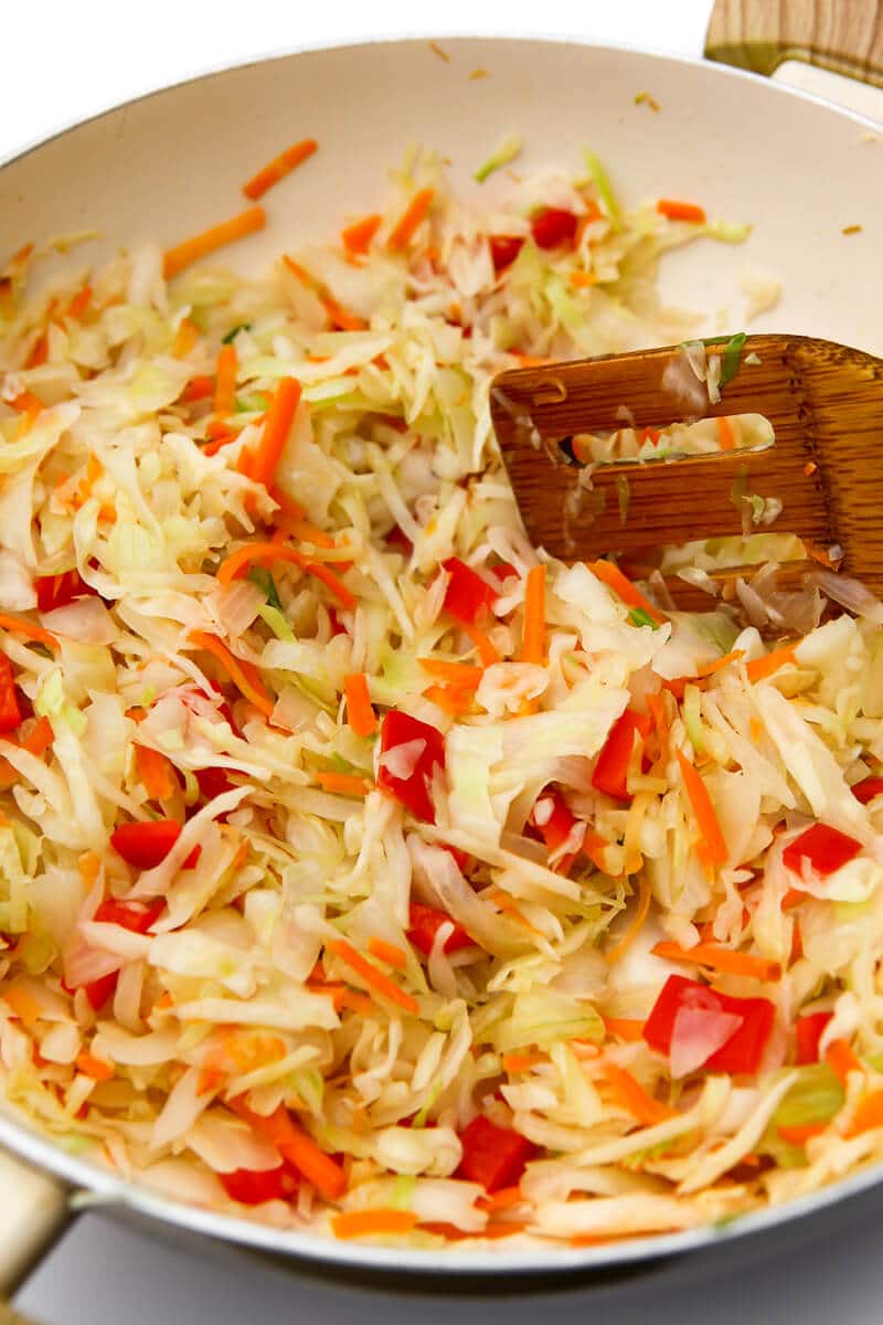  Cabbage, red peppers, onions, and carrots stir-fried in a white wok.