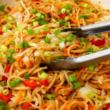 A close up of vegan Hakka noodles being stirred with tongs.