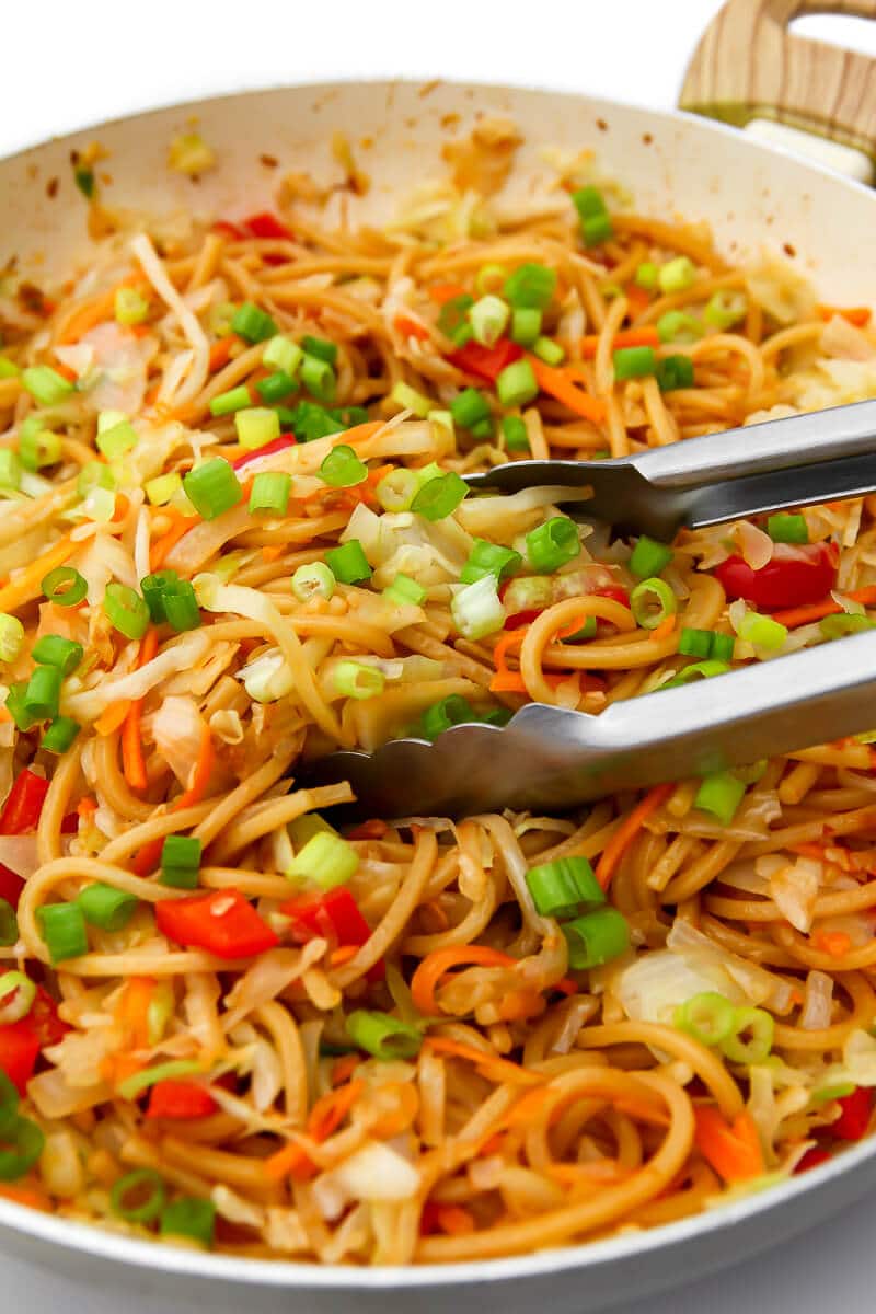 A wok full of vegetable Hakka noodles with cabbage, red peppers, and green onions.