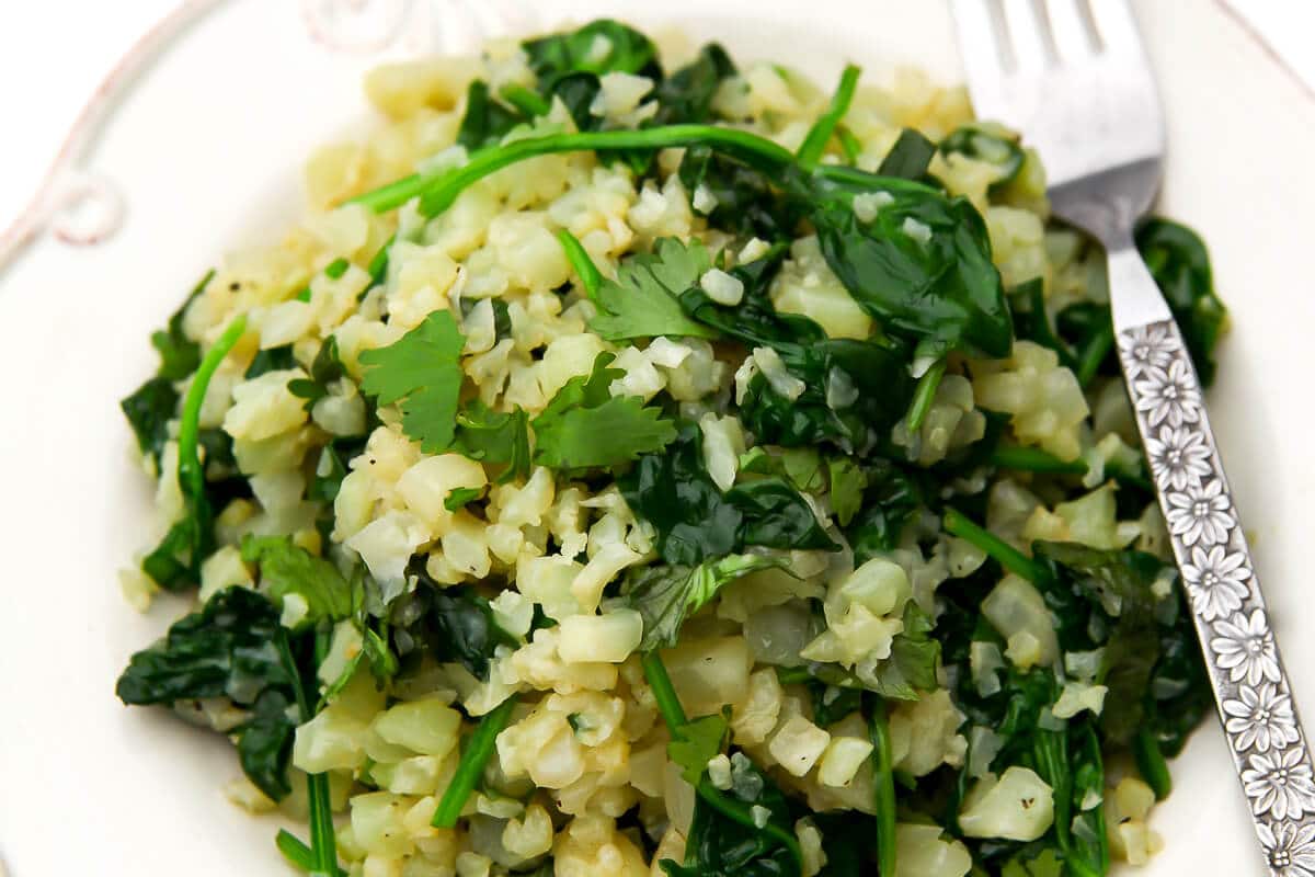 A close up of a plated full of riced cauliflower and sauted spinach and garlic.