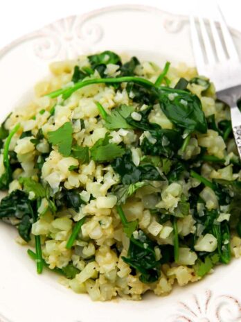 Riced cauliflower risotto with spinach on a white plate with a fork on the side.