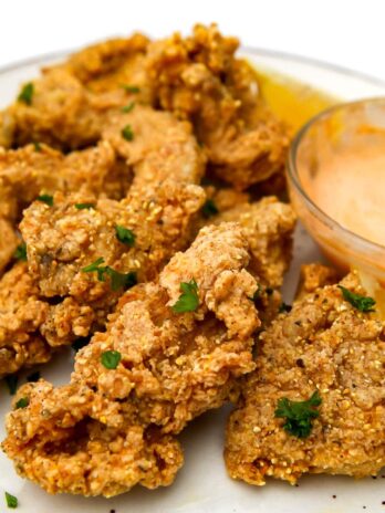 A white plate with deep-fried oyster mushrooms with vegan chipotle mayo on the side.