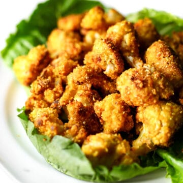 A plate of baked cauliflower nuggets with a crunchy coating on a bed of lettuce.
