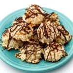A pile of vegan coconut macaroon cookies with chocolate drizzled on top piled on a blue plate.