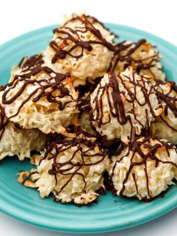 A pile of vegan coconut macaroon cookies with chocolate drizzled on top piled on a blue plate.