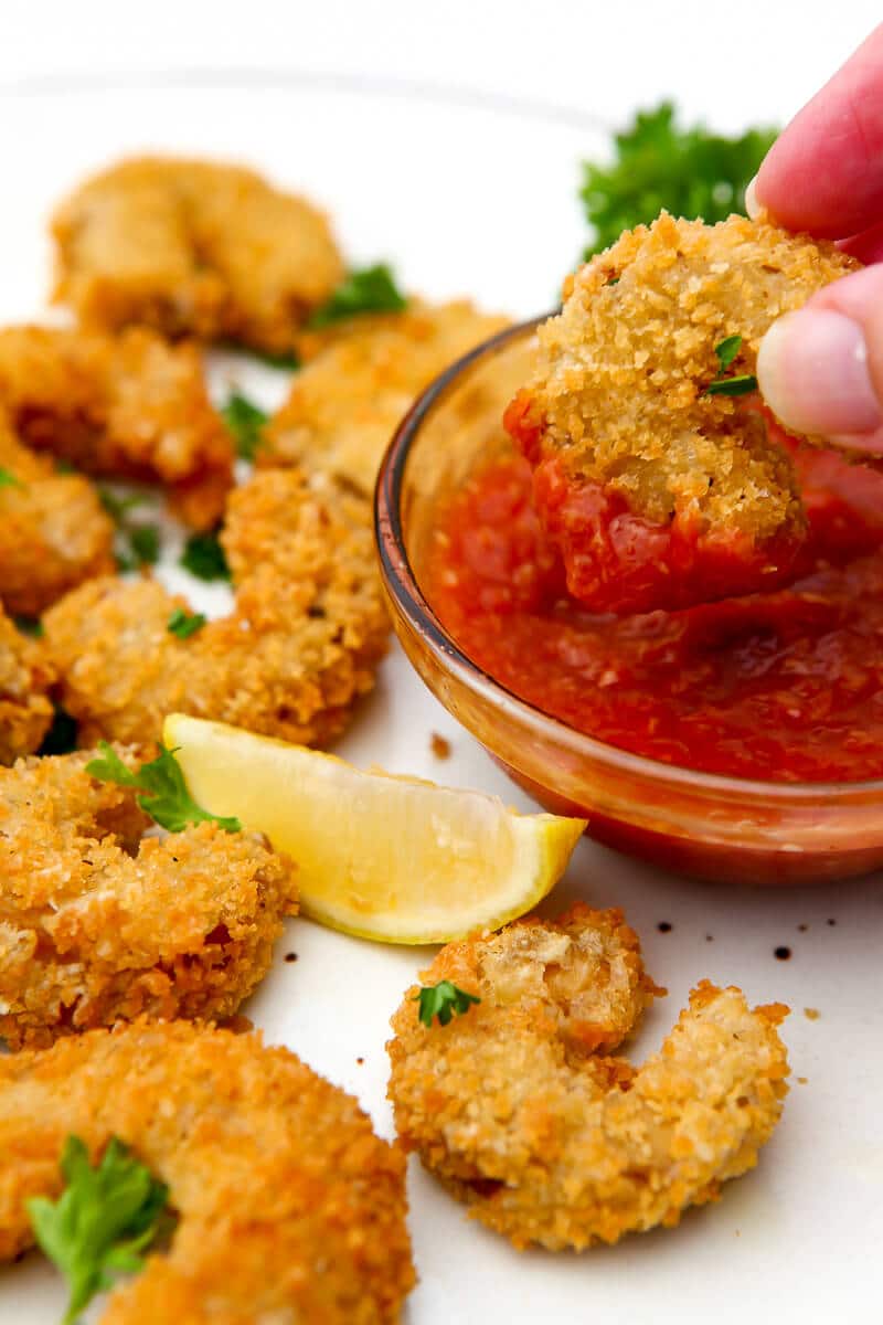 Deep fried vegan shrimp being dipped in cocktail sauce.