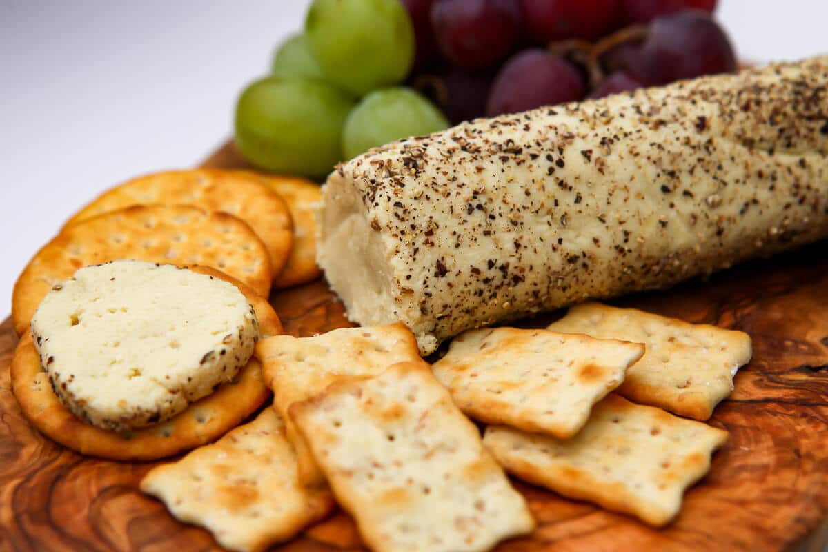 A cutting board with dairy-free goat cheese with crackers and grapes.