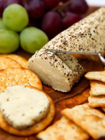 Vegan goat cheese rolled in cracked peppercorn and being slice and put on crackers.