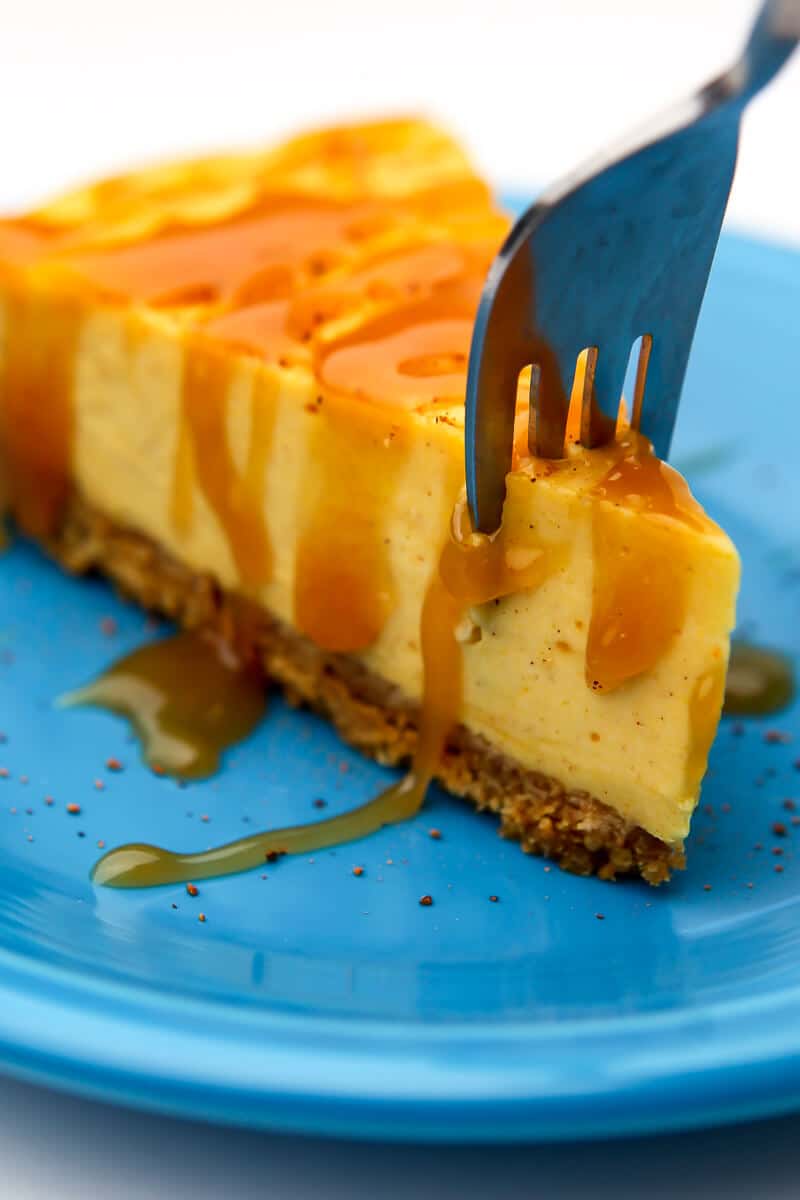 A dairy-free pumpkin cheesecake with caramel on top with a fork in it taking off a piece.
