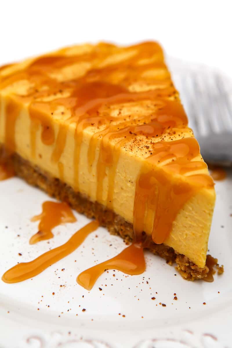 A vegan no-bake pumpkin cheesecake on a white plate with caramel and nutmeg sprinkled on top.