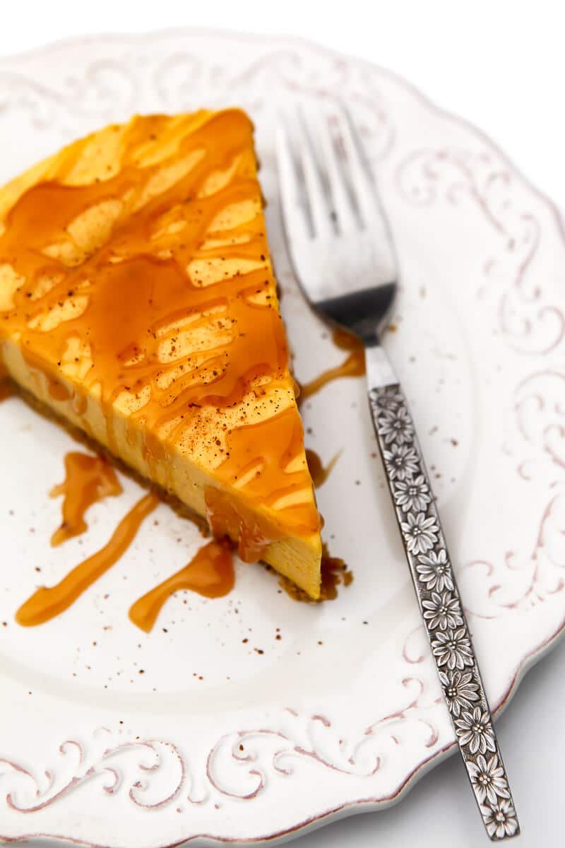 A top view of a vegan pumpkin cheesecake on a white plate with caramel drizzle and a fork on the side.