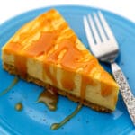 A slice of vegan pumpkin cheesecake on a blue plate with caramel drizzled on top.