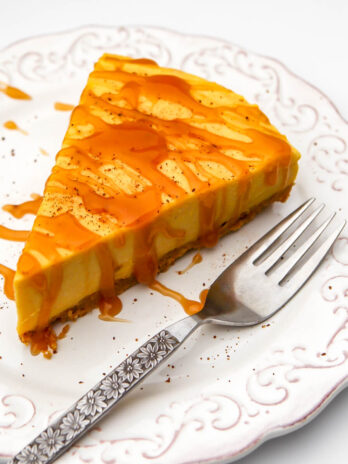 A slice of vegan pumpkin cheesecake on a white plate with caramel drizzled on top.