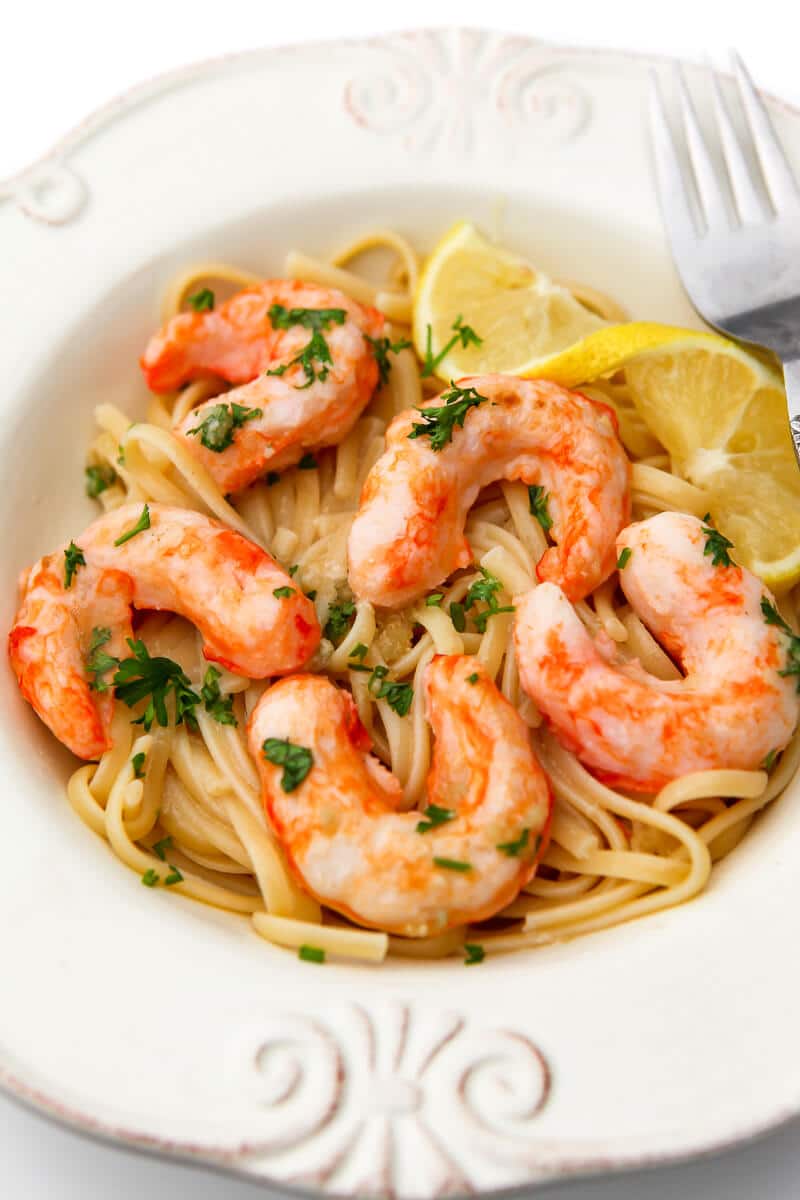 Vegan shrimp scampi in a white bowl with a slice of lemon on the side.