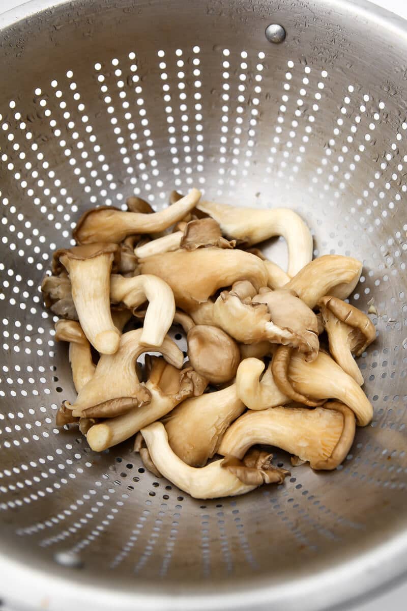 Oyster mushrooms being washed in a metal colander. 