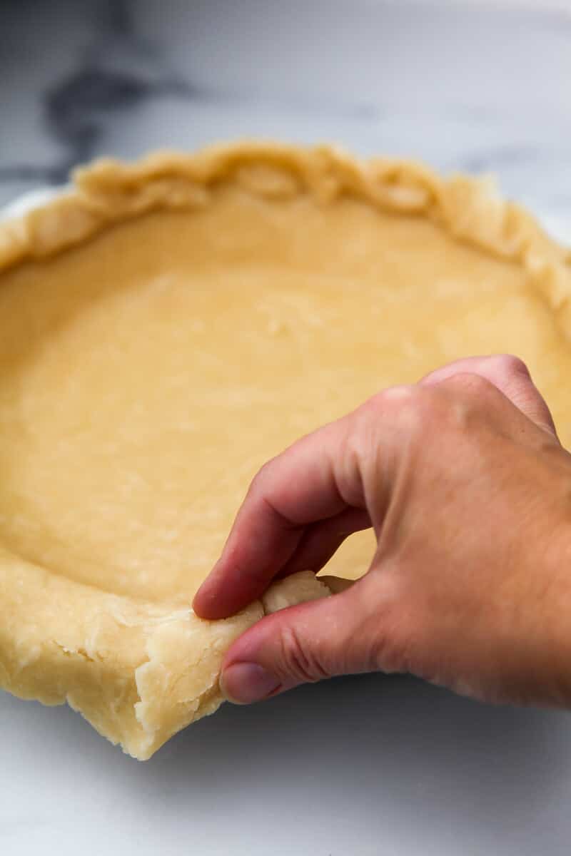 Someone pinching up the edges of a hot water pie crust.