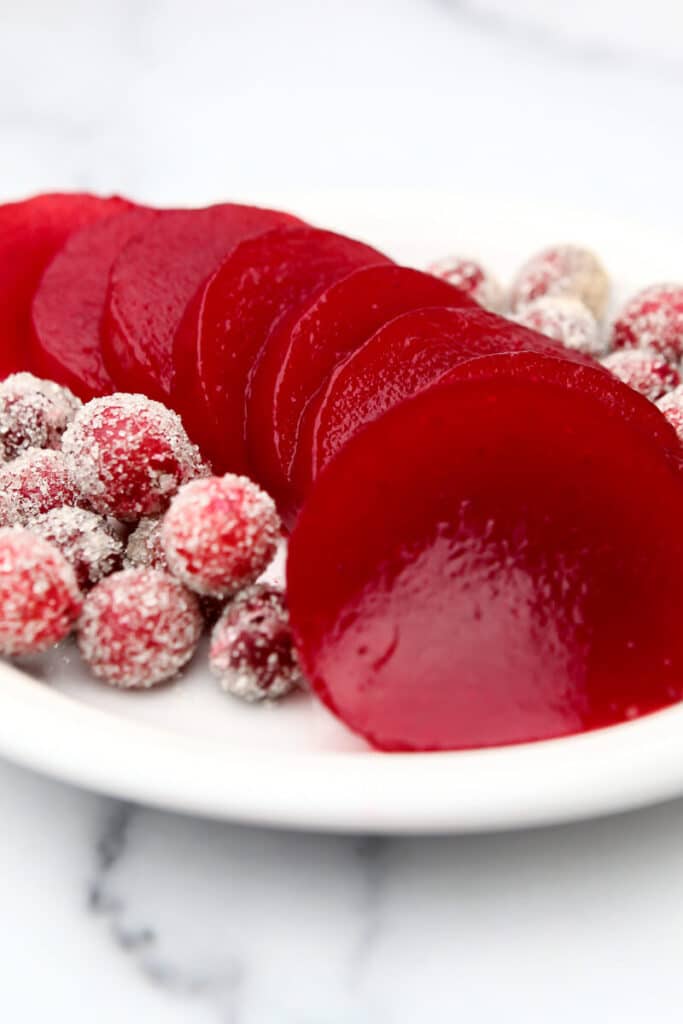 Jellied cranberry sauce cut into slices on a plate with sugared cranberries on the side.