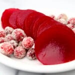 Sliced jellied cranberry sauce on a white plate with sugared cranberries on the side.