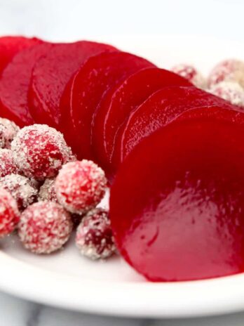 Sliced jellied cranberry sauce on a white plate with sugared cranberries on the side.
