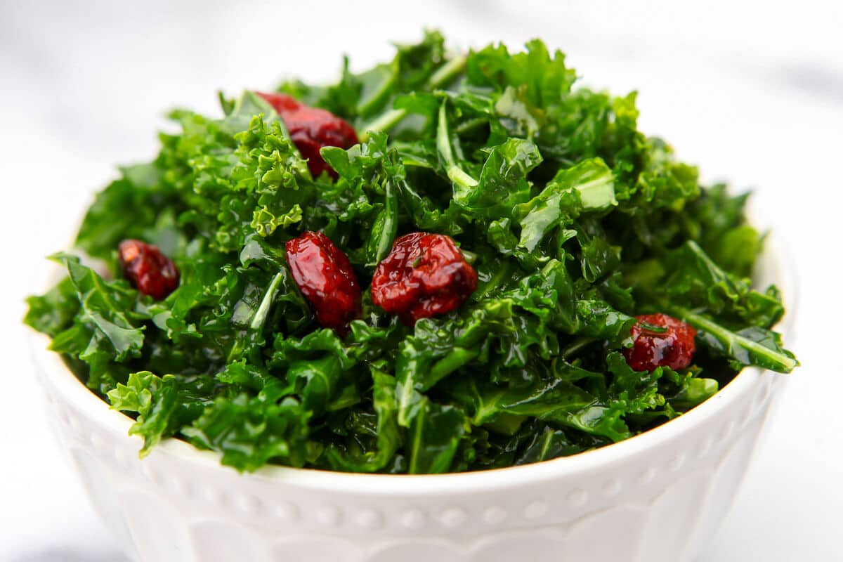 A white bowl filled with a kale salad with dried cranberries mixed in.