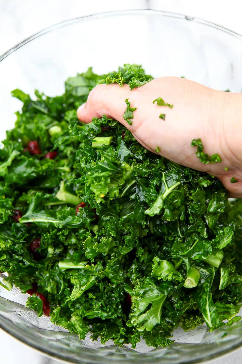 A hand massaging the kale in a cranberry kale salad.