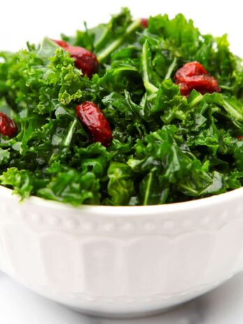 A white bowl filled with vegan kale salad with cranberries and a maple balsamic dressing.