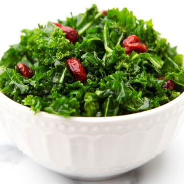 A white bowl filled with vegan kale salad with cranberries and a maple balsamic dressing.