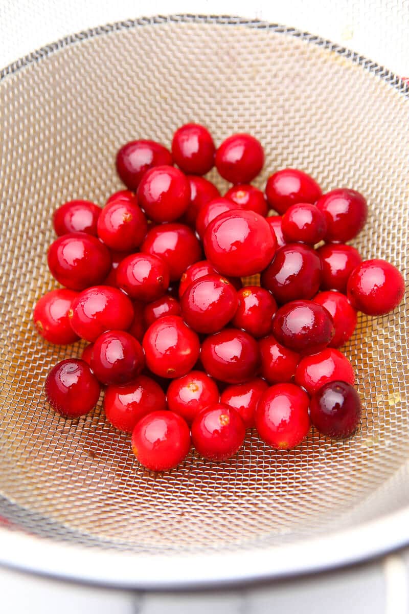 Cranberries in a metal strainer to drip off syrup before rolling in sugar.