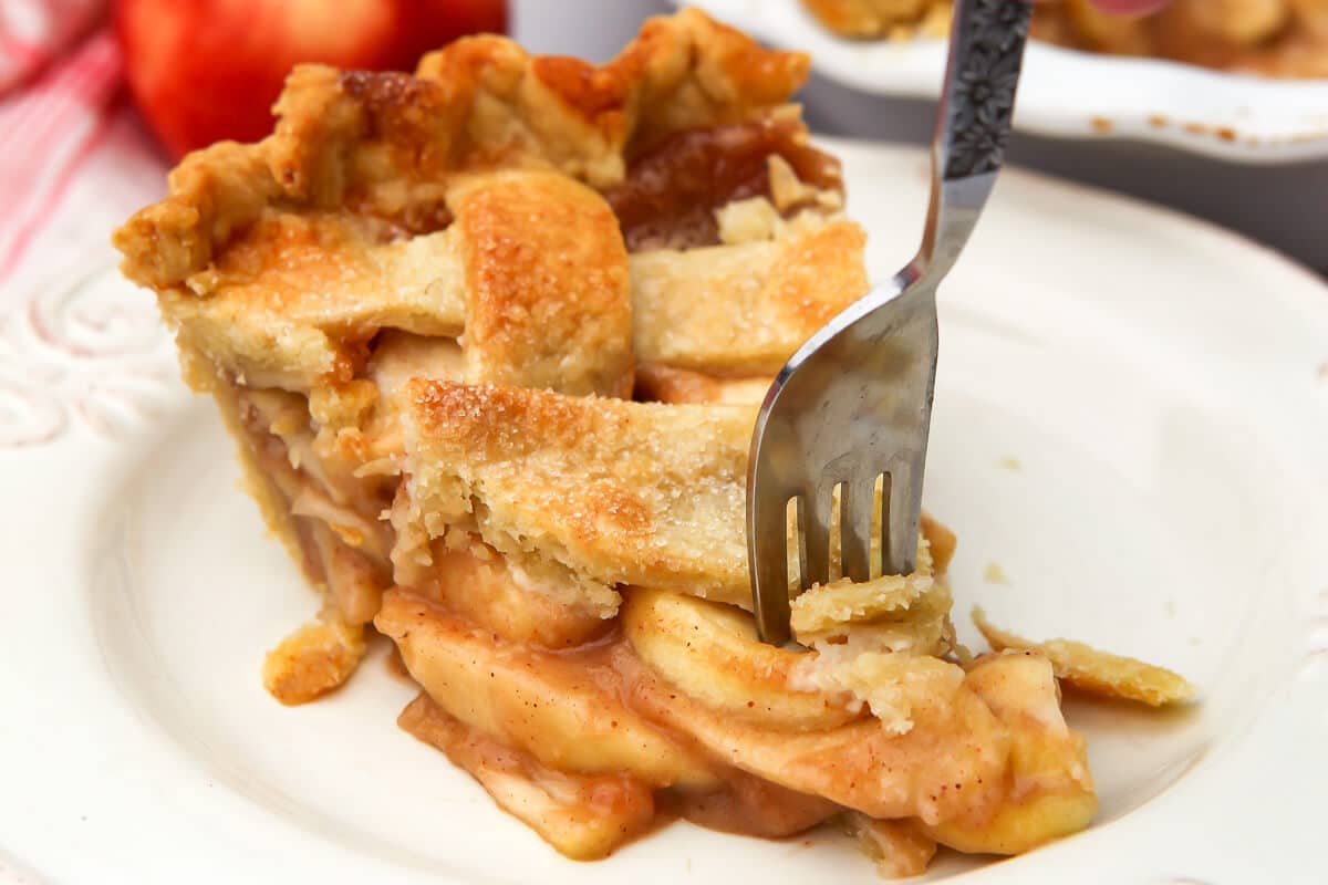A piece of a vegan apple pie on a white plate with a fork sticking in it.
