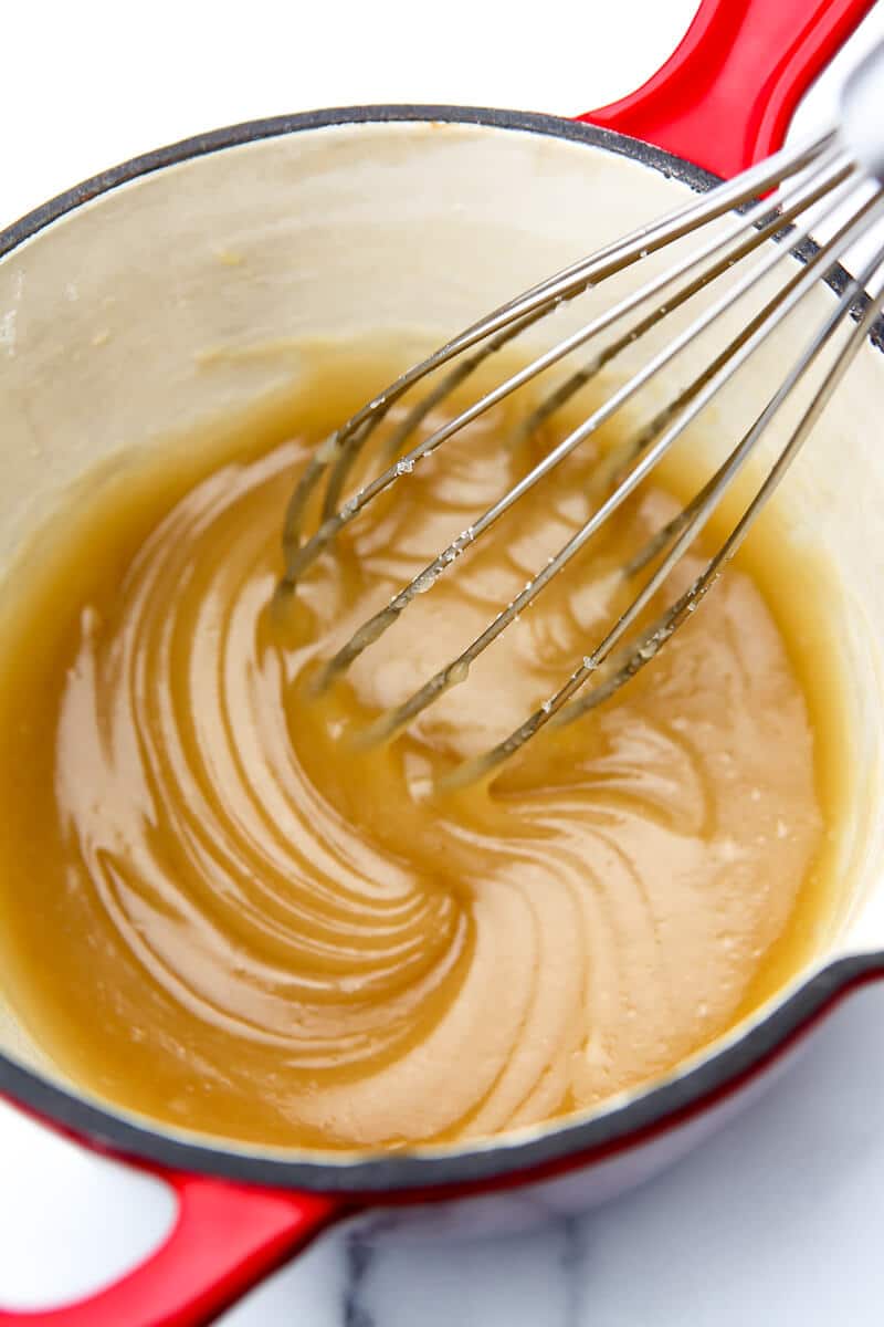 A small red sauce pan with a vegan apple pie filling sauce being stirred with a whisk.
