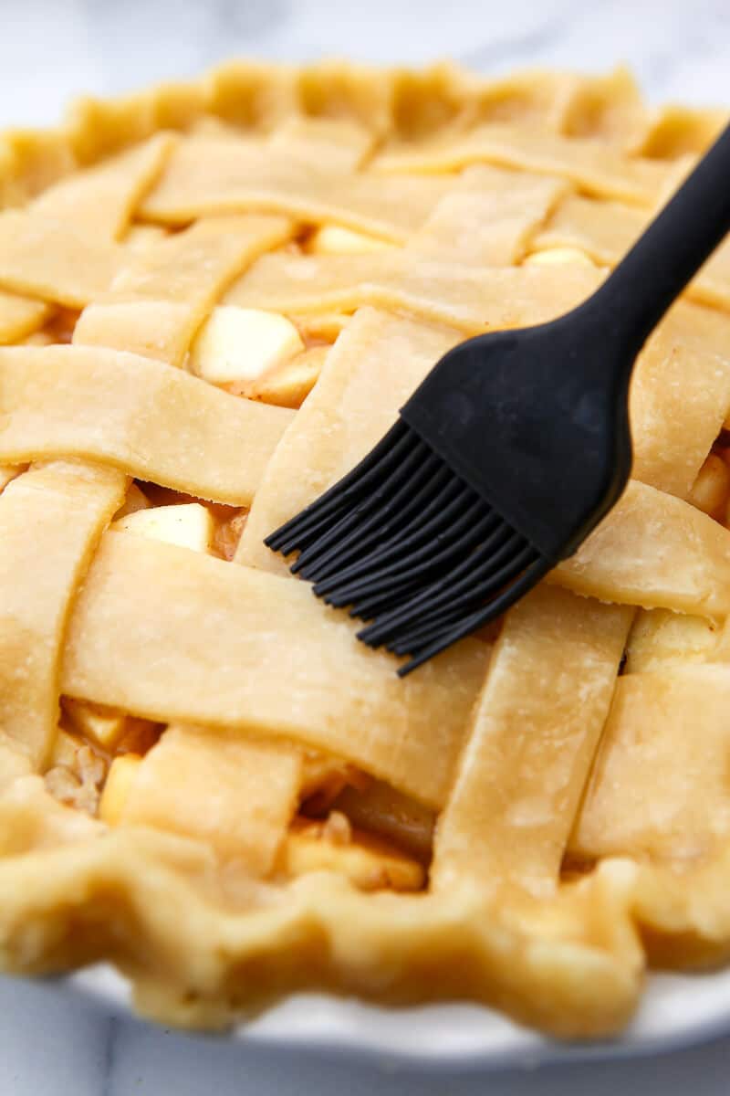 Brushing the top of a vegan apple pie with a vegan egg wash before baking.