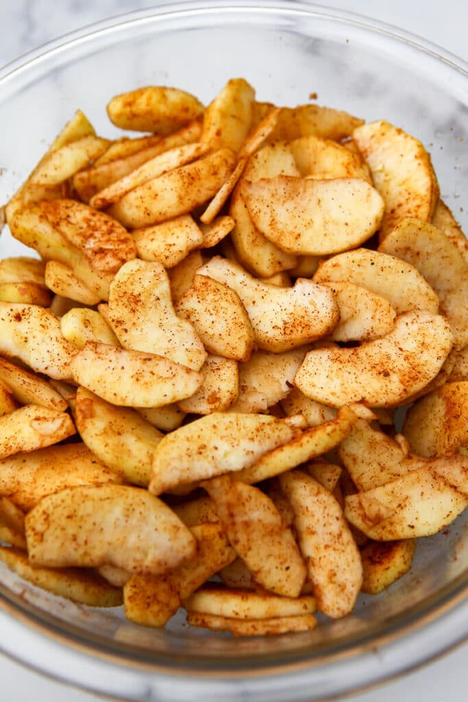 Apples in a mixing bowl sprinkled with cinnamon and nutmeg.
