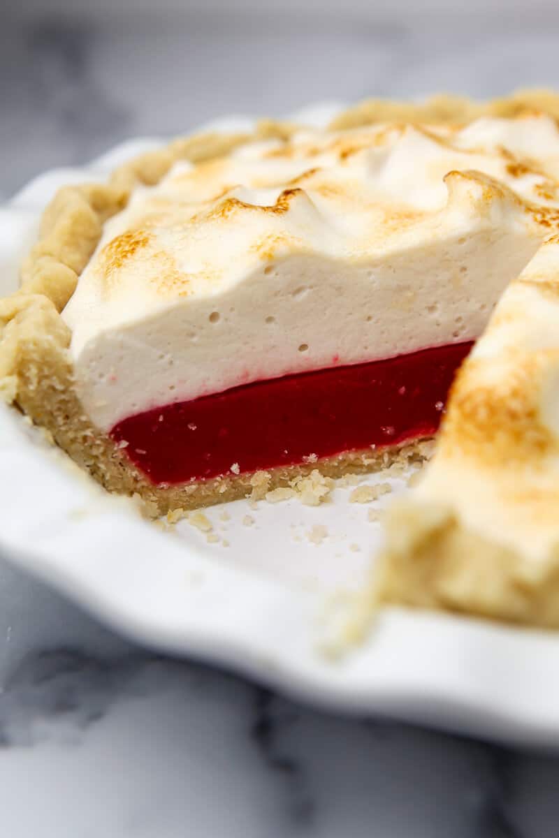 A vegan cranberry meringue pie with a toasted top and a slice taken out of it.