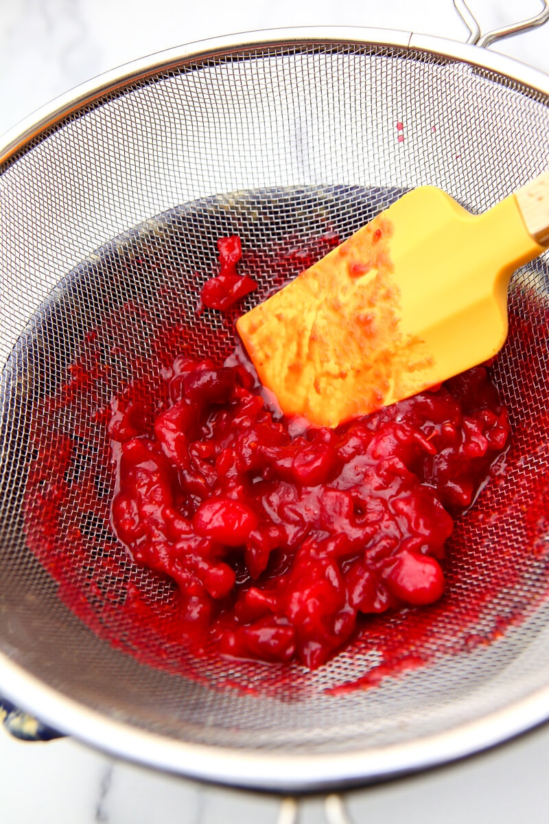 Straining cranberry sauce through a mesh strainer.