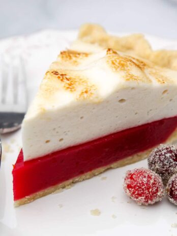 A vegan cranberry meringue pie on a white plate with a fork and sugared cranberries on the side.