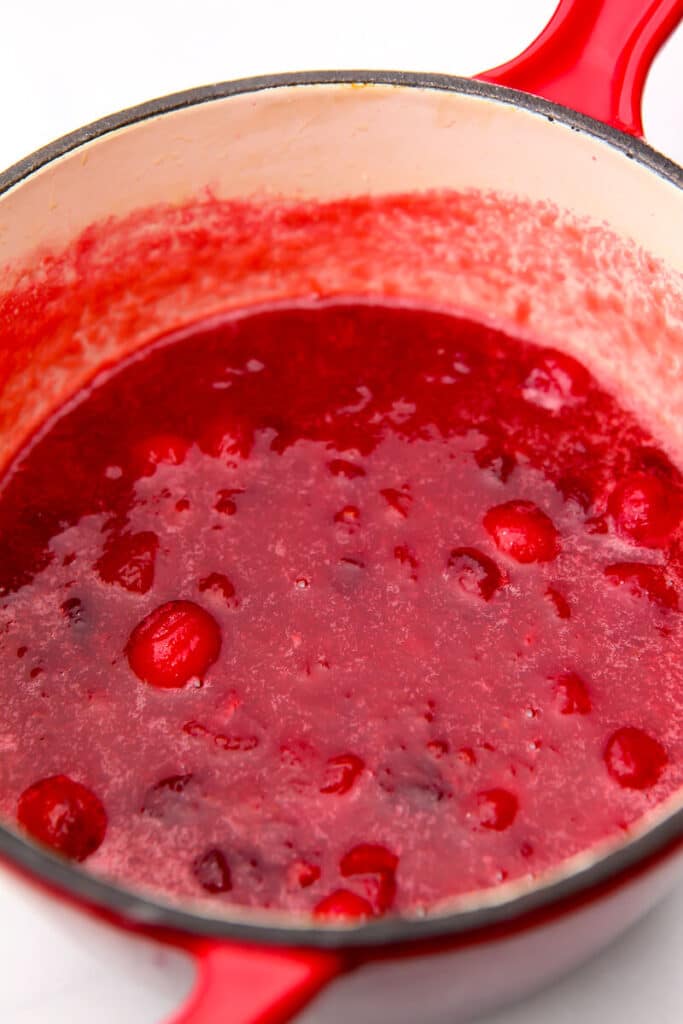 A small red saucepan filled with cranberries cooked in orange juice until they have popped open and have made a sauce.