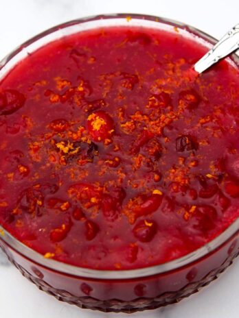 A glass bowl filled with vegan cranberry sauce with orange zest on top.