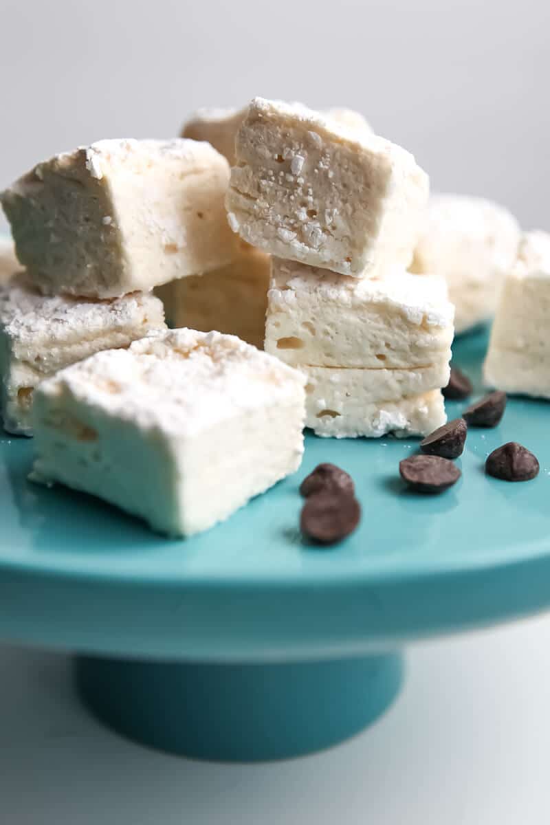 Homemade vegan marshmallows on a blue cake pan with chocolate chips around them.