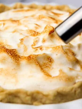 A pie with vegan meringue being toasted with a kitchen torch.