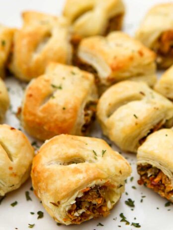 A white plate full of vegan sausage rolls with some parsley sprinkled on top.