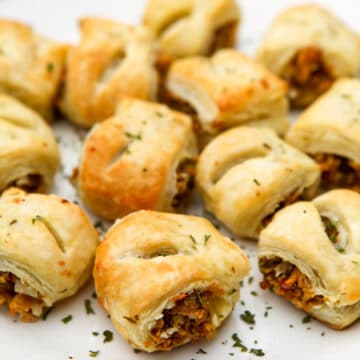 A white plate full of vegan sausage rolls with some parsley sprinkled on top.