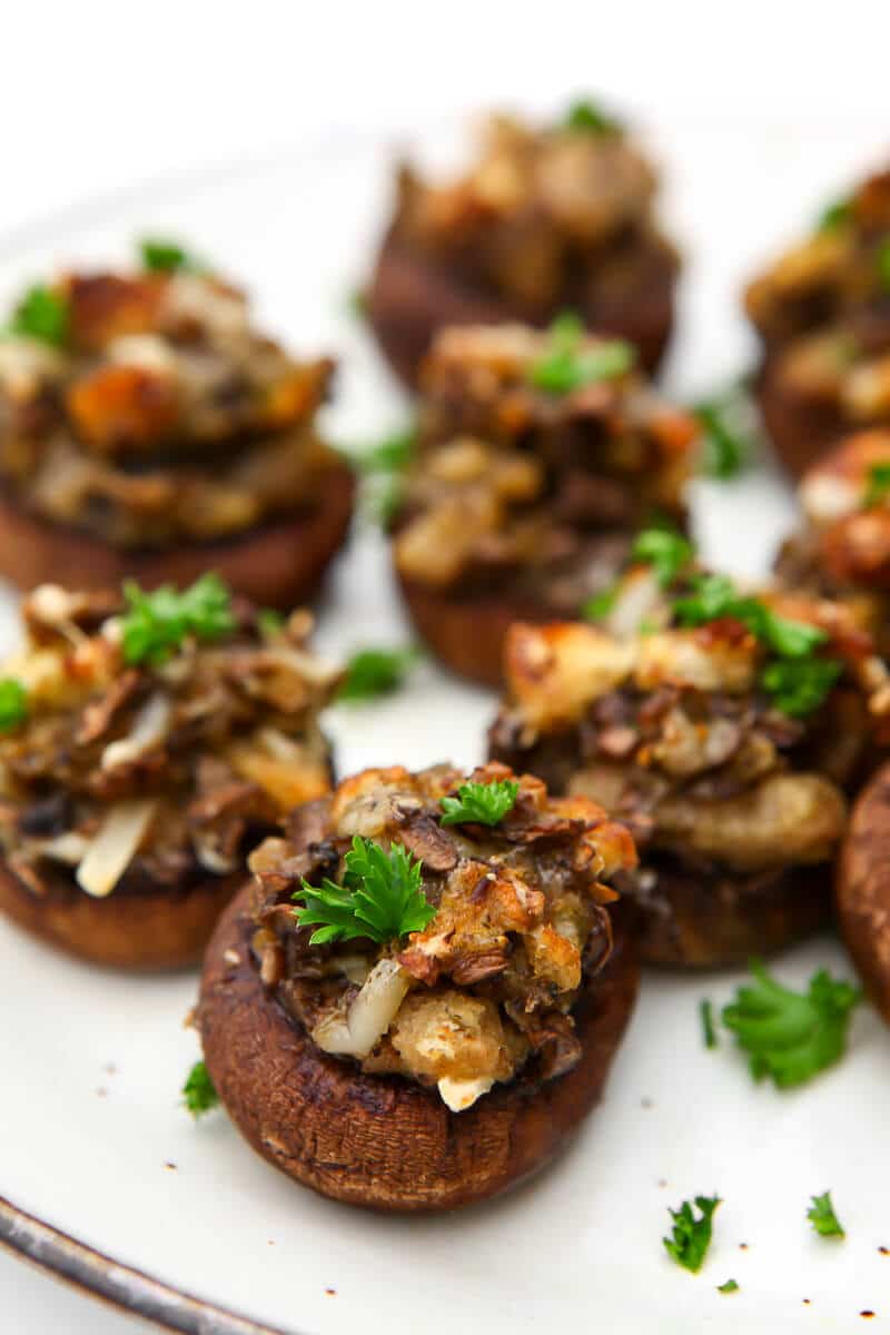 Vegan stuffed mushrooms on a white plate with parsley sprinkled on them.