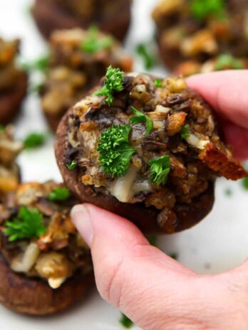 A person picking up a stuffed mushroom off a plate of them.