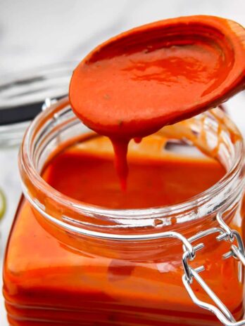 A vegan New Mexico style red chile sauce in a glass jar with some sauce dripping off a spoon.
