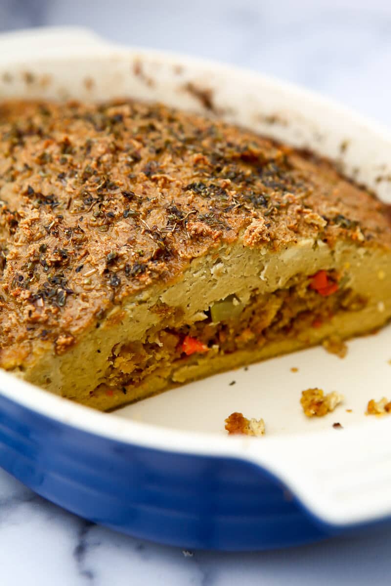 A gluten-free vegan tofu turkey with stuffing in the middle baked in a blue baking dish.