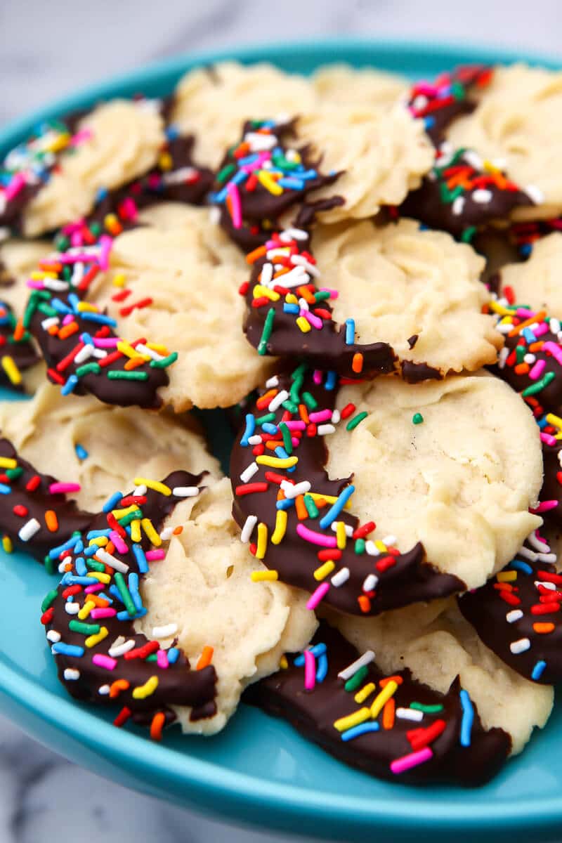A blue plate filled with vegan butter cookies with one side dipped in chocolate and covered in sprinkles.
