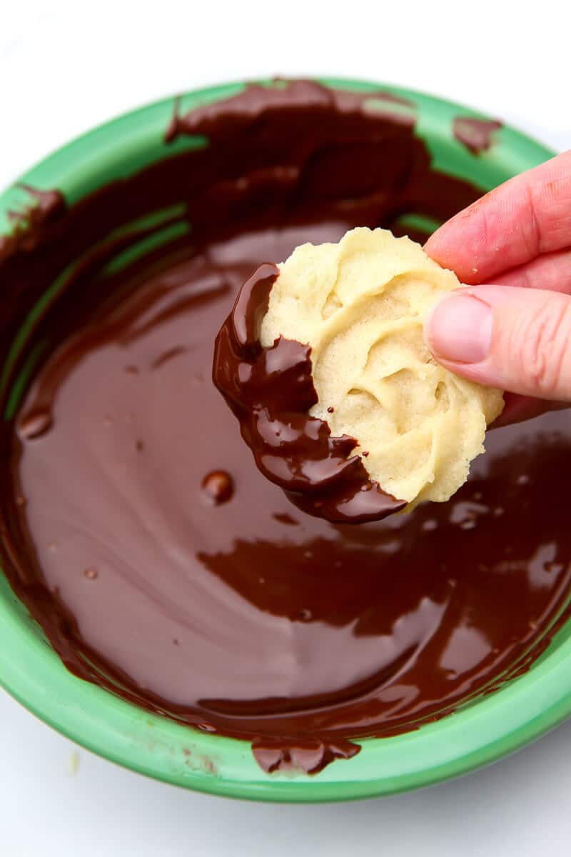 Someone dipping part of a danish butter cookie into melted chocolate.