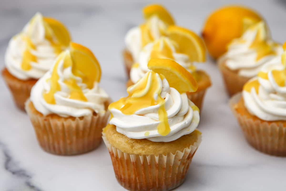 Vegan lemon cupcakes with frosting and lemon curd on a marble countertop.