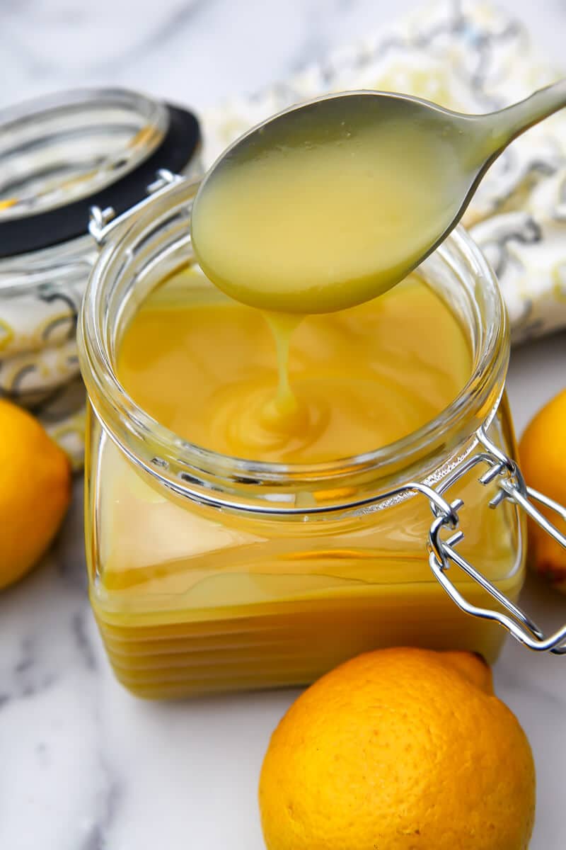 A glass jar filled with vegan lemon curd with lemons on the side.